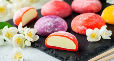 Multi-colored Japanese ice cream Mochi in rice dough and Jasmine flowers on a concrete blue background. Traditional Japanese dessert on a black slate.