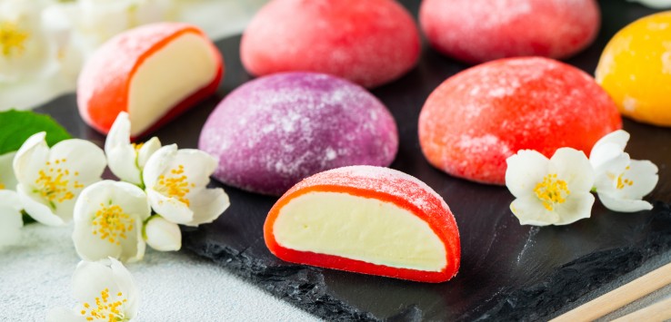 Multi-colored Japanese ice cream Mochi in rice dough and Jasmine flowers on a concrete blue background. Traditional Japanese dessert on a black slate.