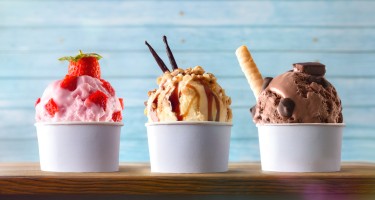 Three glasses of ice cream with strawberry, vanilla and chocolate balls decorated on a wooden table and blue slatted background. Front view.