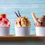 Three glasses of ice cream with strawberry, vanilla and chocolate balls decorated on a wooden table and blue slatted background. Front view.