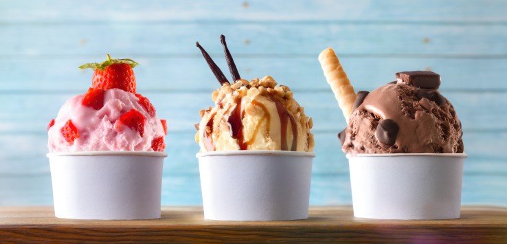 Three glasses of ice cream with strawberry, vanilla and chocolate balls decorated on a wooden table and blue slatted background. Front view.