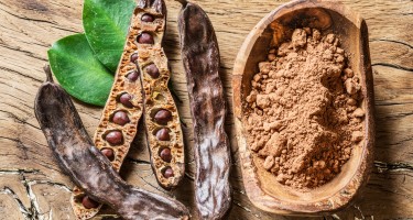 Carob pods and carob beans on the wooden table.