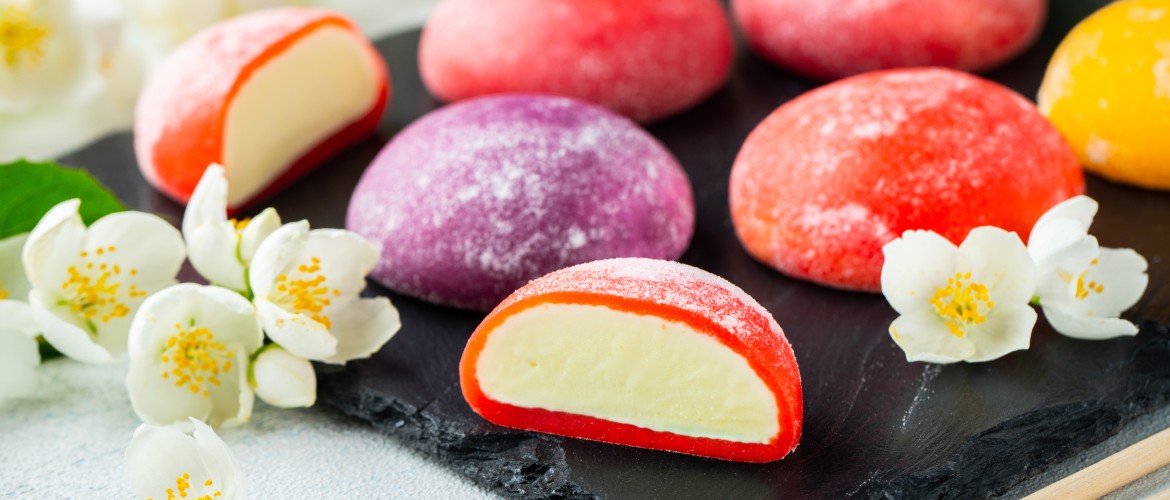 Multi-colored Japanese ice cream Mochi in rice dough and Jasmine flowers on a concrete blue background. Traditional Japanese dessert on a black slate.