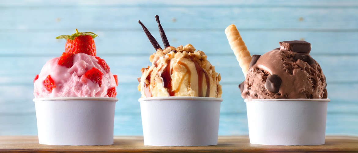 Three glasses of ice cream with strawberry, vanilla and chocolate balls decorated on a wooden table and blue slatted background. Front view.